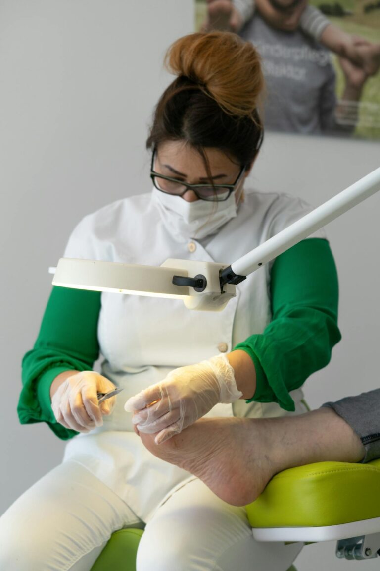 Concentrated skilled specialist wearing medical uniform doing procedure on leg of crop customer under light of lamp