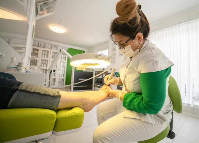 Side view of serious female in medical uniform and mask making hardware pedicure using modern equipment